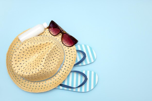 Straw hat sunglasses striped flip flops sun cream on blue background with copy space