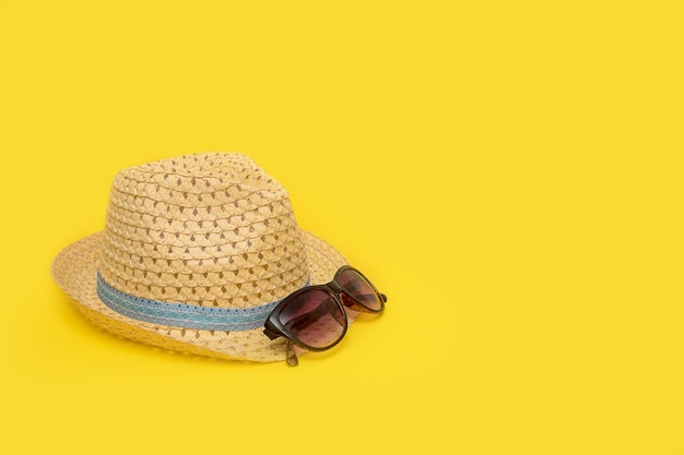 Straw hat and sunglasses on a yellow background with copy space