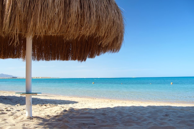 Straw shade umbrella in sea tropical region against blue vibrant sky in summer