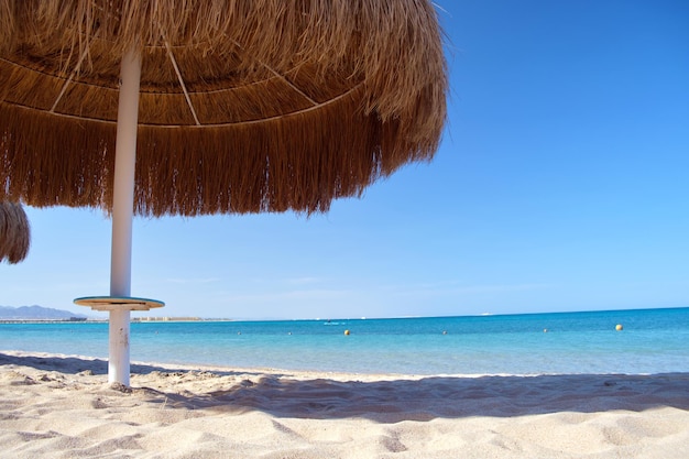 Straw shade umbrella in sea tropical region against blue vibrant sky in summer