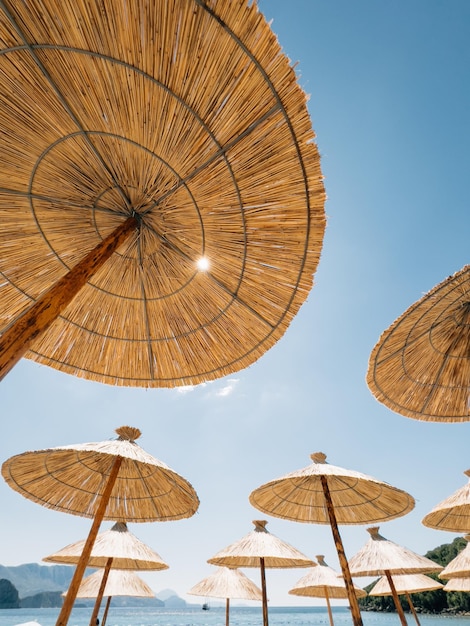 Straw sun umbrellas on the beach by the sea against the blue sky