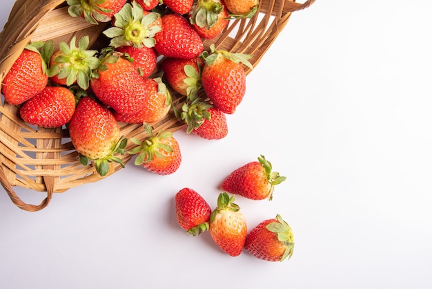 Strawberries, beautiful strawberries dropped from a straw braided basket onto a white surface, selective focus.