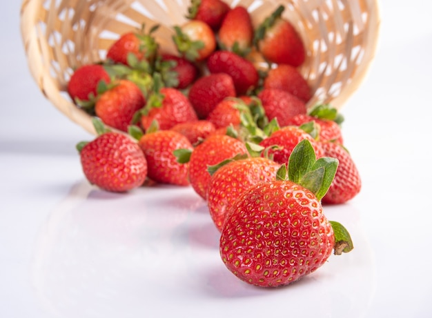 Strawberries, beautiful strawberries dropped from a straw braided basket onto a white surface, selective focus.