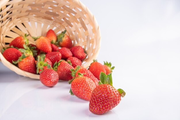 Strawberries, beautiful strawberries dropped from a straw braided basket onto a white surface, selective focus.