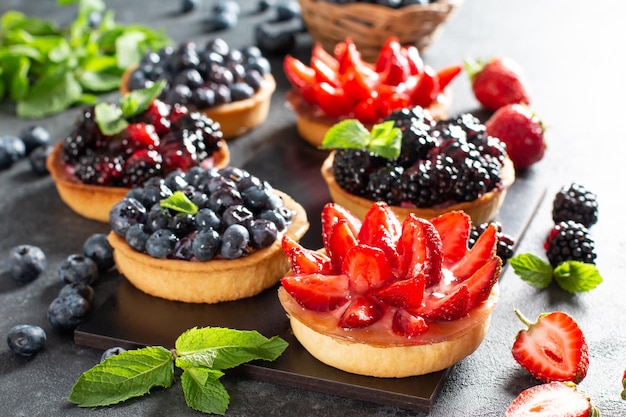 Strawberries, blueberries, blackberries tartlets with chocolate ganache, fresh berries and mint leaves, selective focus. Fresh fruit tart, freshly homemade fruit cake on a table