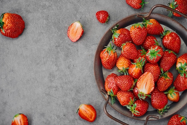 Strawberries and cut ripe berries in a metal dish on a gray concrete table layout with copy space Delicious natural dessert Seasonal juicy berry