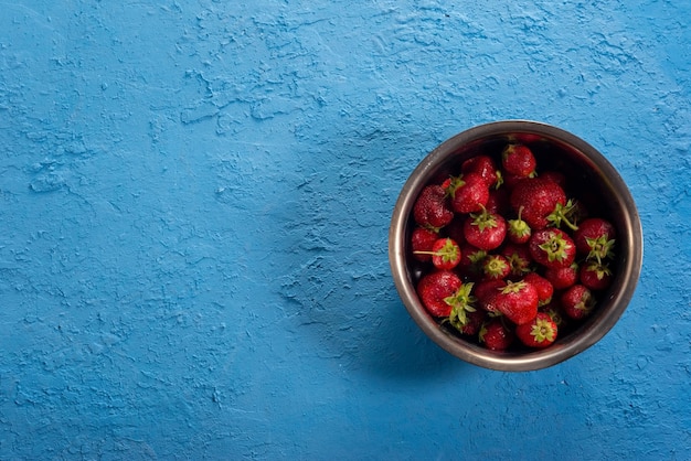 Strawberries in a metal bowl on a blue background View from above