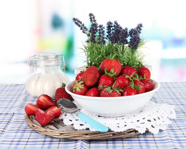 Strawberries in plate on wicker stand on table on window background