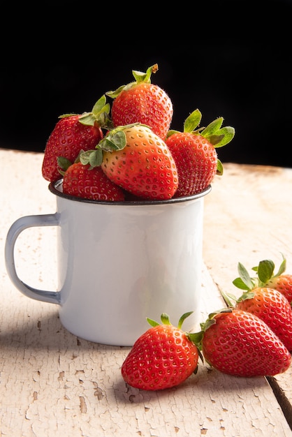 Strawberries, several beautiful strawberries in a white mug and on an old and weathered wooden plank, selective focus.