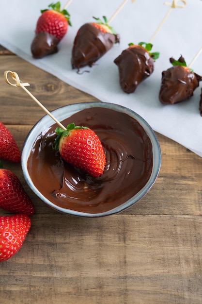 Strawberries with chocolate on a wooden background Strawberries dipping process in chocolate Copy space