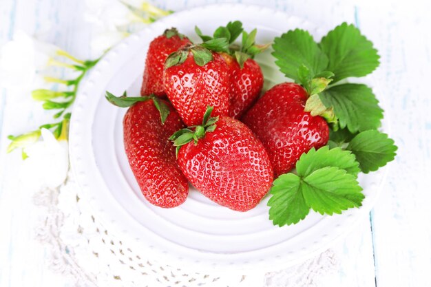 Strawberries with leaves on plate on wooden background