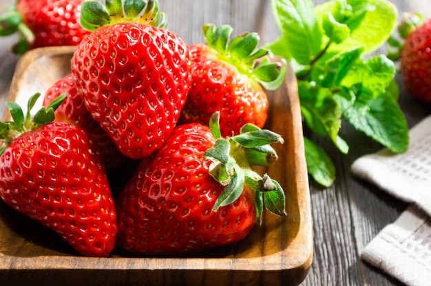 Strawberries in wooden bowl and mint leaves on wooden background.