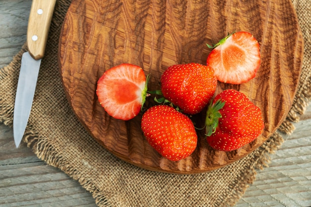 Strawberries on wooden cutting board over burlap napkin and grey wooden