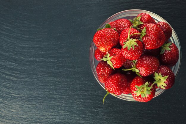 Strawberry in a bowl on a black slate table. Top view, flat lay with copy space