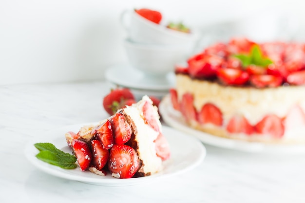 Strawberry cake Fraisier on the white plate and cups for teatime, cutted piece at the foreground