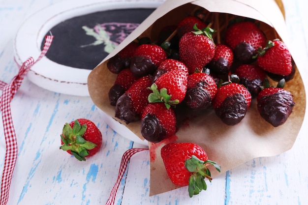 Strawberry in chocolate on skewers in paper bag on table close-up