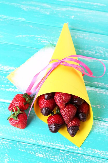 Strawberry in chocolate on skewers in paper bag on table close-up