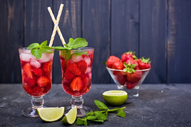 strawberry drink with mint, lime and ice in glasses with straws on a dark background