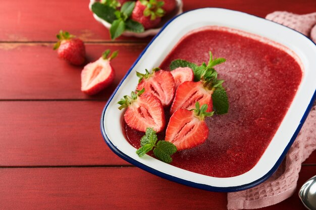 Strawberry granita or fresh berry sorbet in white rustic bowl on old wooden table background Ice cream with strawberry and mint Summer treat Top view