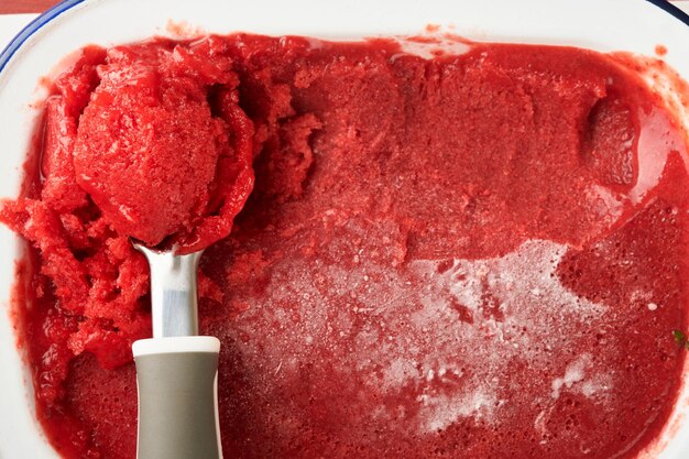 Strawberry granita or fresh berry sorbet in white rustic bowl on old wooden table background Texture of ice cream or sorbet Ice cream with strawberry and mint Summer treat Top view