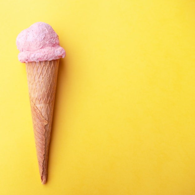 Strawberry ice cream in waffles cone on yellow background.