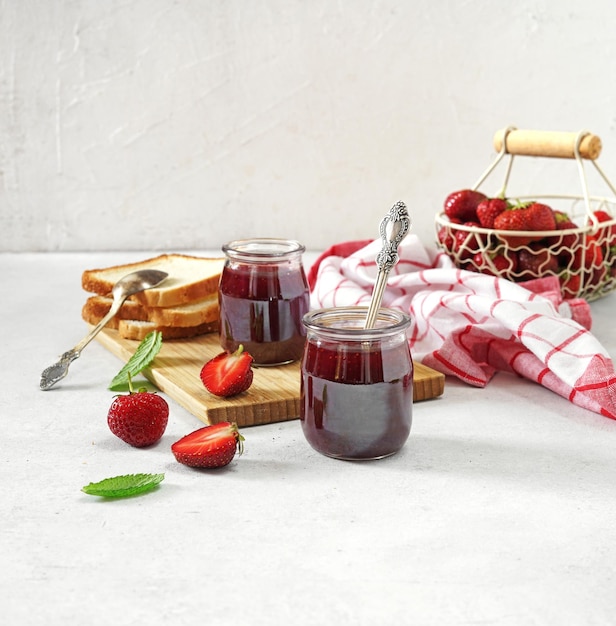 Strawberry jam in the glass jar at white table