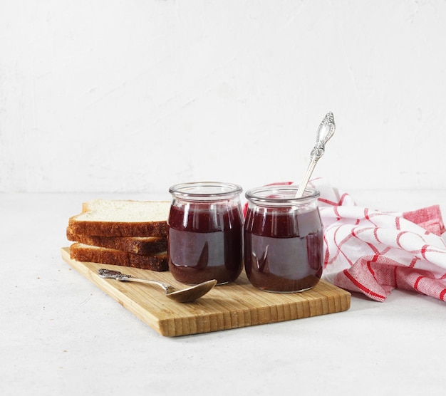 Strawberry jam in two glass jars at white table copy space