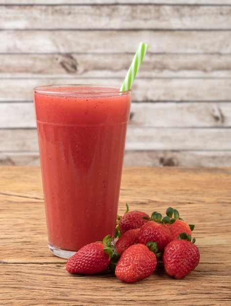 Strawberry juice in a glass with fruits over wooden table.