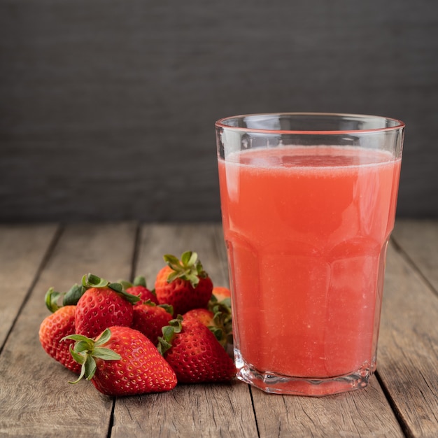 Strawberry juice in a glass with fruits over wooden table.