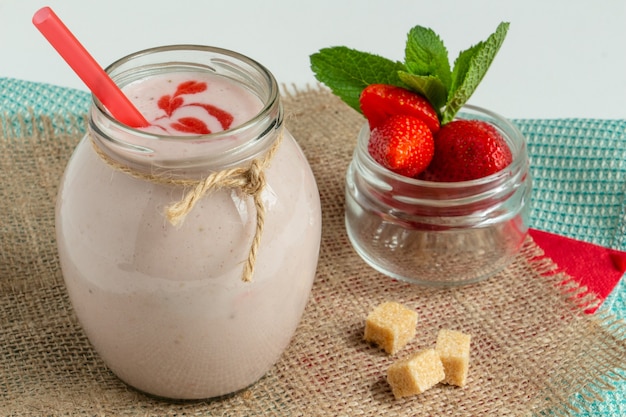 Strawberry milkshake in a jar with strawberries and mint sprigs