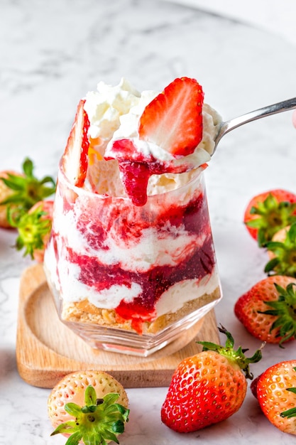 Strawberry mousse cake in a glass placed on a marble table The distinctly layered strawberry mousse cake is beautifully decorated with sliced fresh strawberries