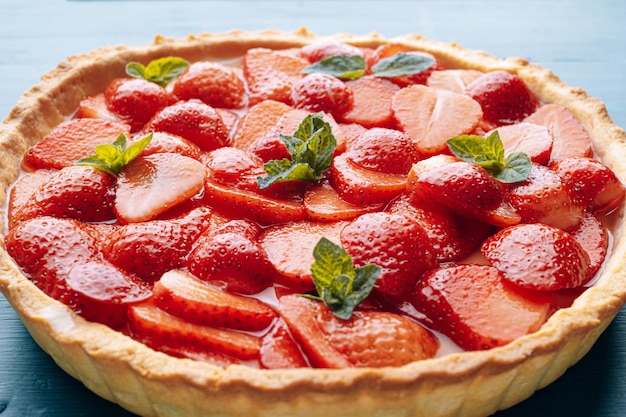 Strawberry quiche with lime zest and strawberry slices laid on top and topped with lime jelly on a blue wooden table