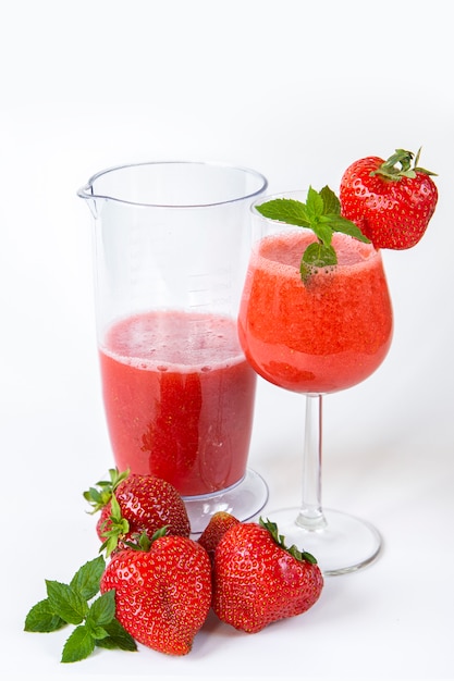 Strawberry smoothie in a glass on a high leg decorated with strawberries and mint on white