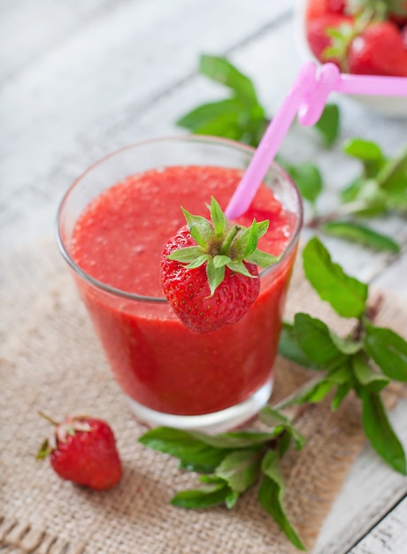 Strawberry smoothie in glass and mint leaves on a wooden surface in rustic style