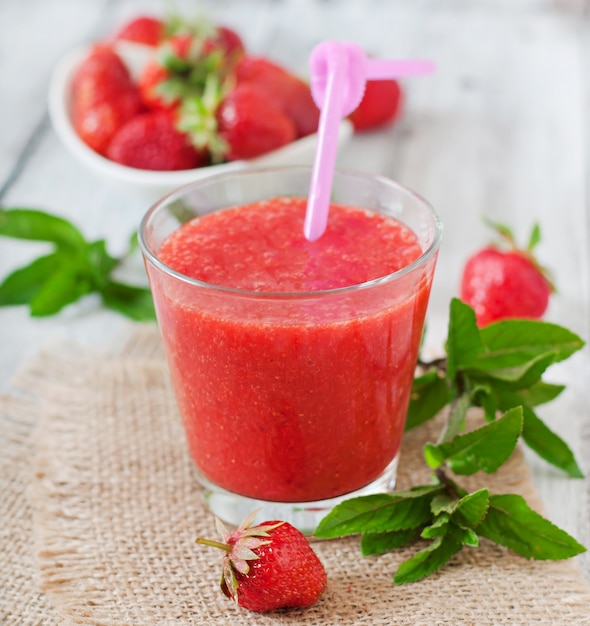 Strawberry smoothie in glass and mint leaves on a wooden surface in rustic style