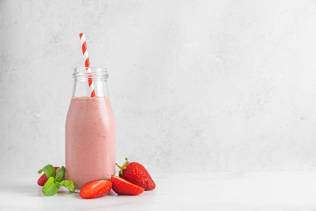 Strawberry smoothie or milkshake in a glass bottle with straw and mint on white background