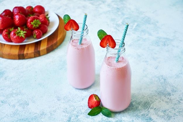 Strawberry smoothie or milkshake in glass jar with berries on blue concrete background