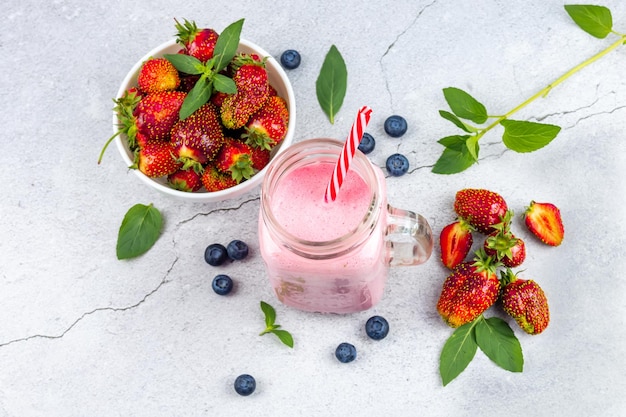 Strawberry smoothie or milkshake with berries in a glass jar on a gray concrete background Vegetarian healthy drink