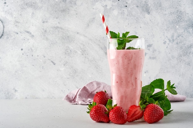 Strawberry smoothie or milkshake with berries and mint in tall glass on light grey background. Summer drink shake, milkshake and refreshment organic concept. Place for text.