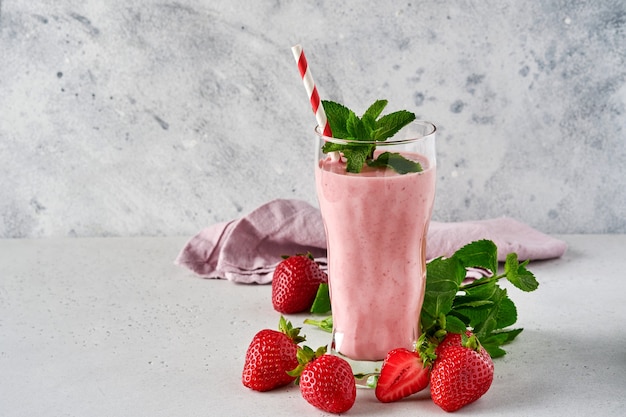 Strawberry smoothie or milkshake with berries and mint in tall glass on light grey background. Summer drink shake, milkshake and refreshment organic concept. Place for text.