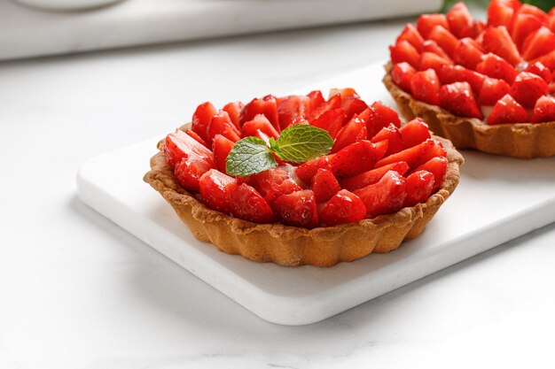 Strawberry tarts with vanilla cream on white board and white background close up