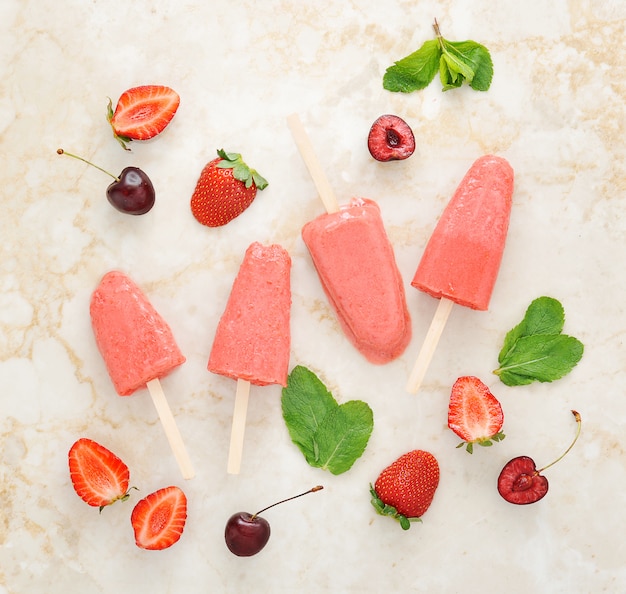 Strawberry yogurt ice cream popsicles with mint and cherry over marble tray