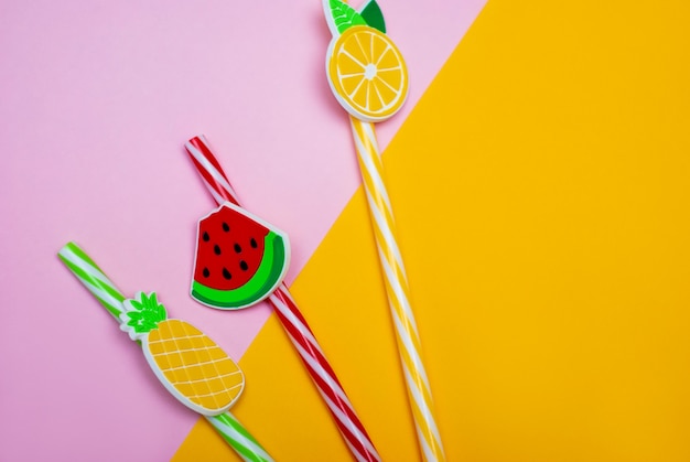 Straws in shape of watermelon, lemon and pineapple on a pink and yellow background