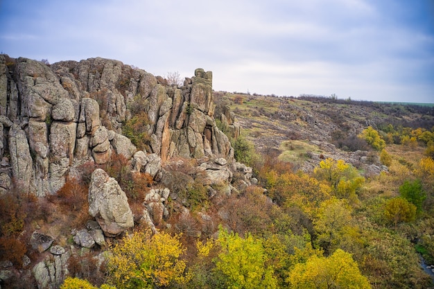 A stream flows in the Aktovsky Canyon, Ukraine. Autumn trees and large stone boulders around. Aerial panoramic drone shot