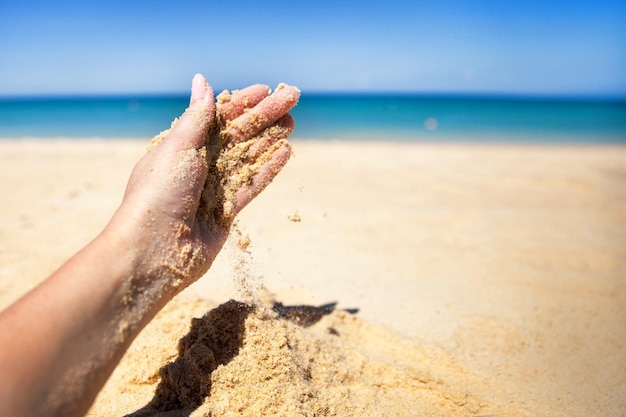 A stream of sand falls from the hand of a woman on a sandy beach