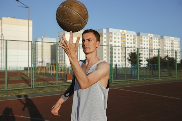 Street ball male player spinning basketball on finger while standing on urban playground in summer