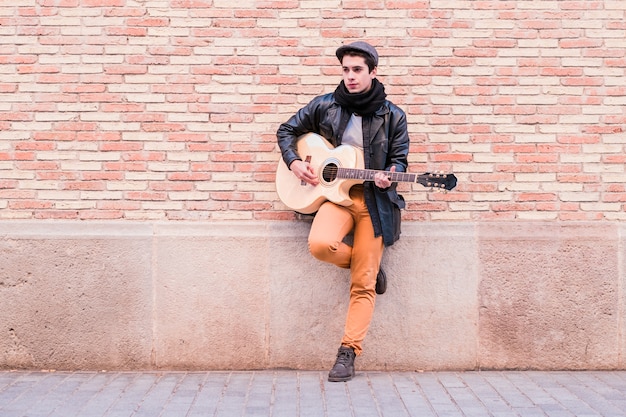 Street musician playing acoustic guitar Young handsom man wearing coat and hat outdoors