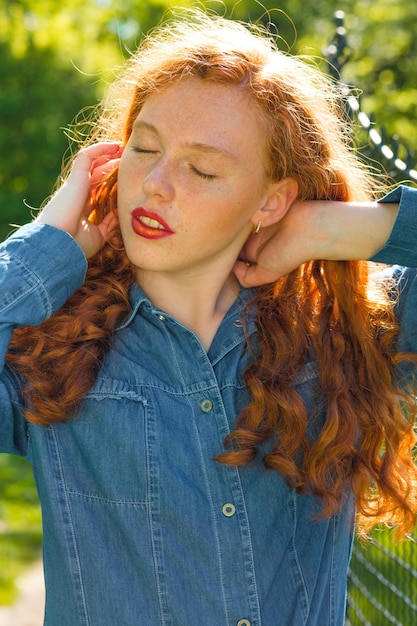 Street portrait of attractive red haired model with closed eyes posing at the park