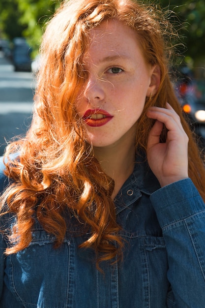 Street portrait of red haired model in blue jeans shirt in rays of sun at the street