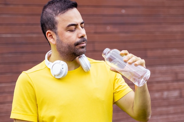 Street portrait young athlete man in yellow tee earphones on neck wooden wall posing outdoors